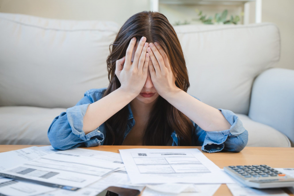 young person with head in hands sitting in front of multiple bills