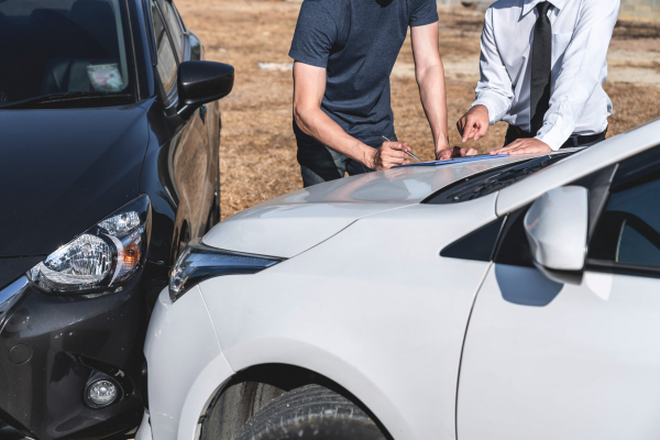 Two people filling out paperwork by two cars that crashed together