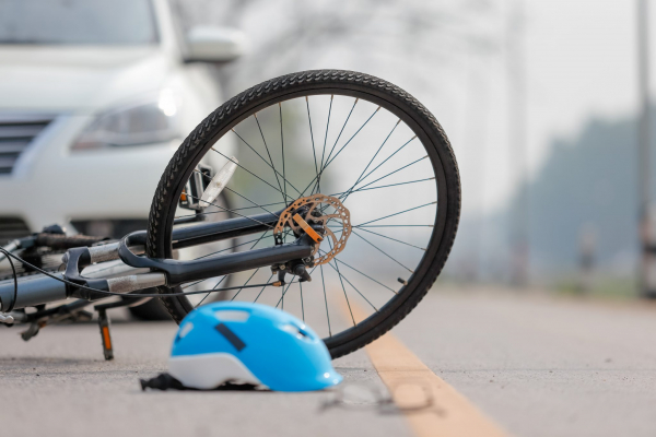 bike and bike helmet on the ground in front of a stopped car 