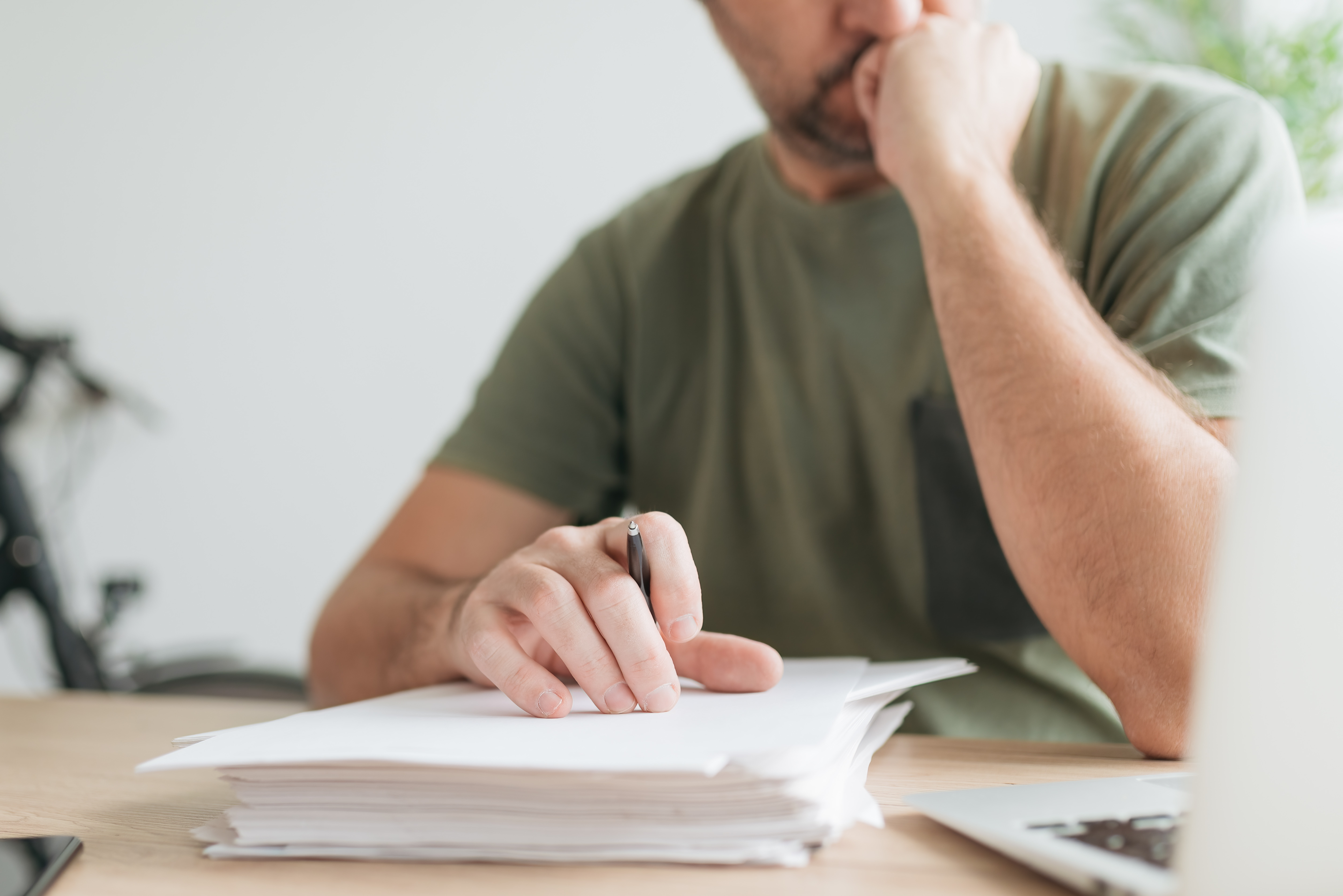 person looks pensively at a down a desk with a large stack of papers on it